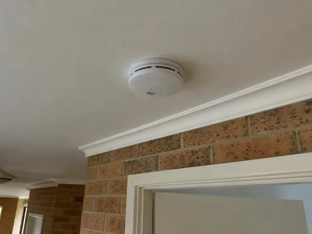 Ceiling-mounted smoke alarm above a brick doorway in a home interior in Thornton
